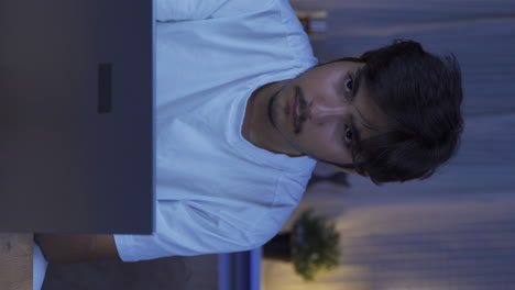Vertical-video-of-Man-focusing-on-computer-has-serious-expression.-At-home-at-night.